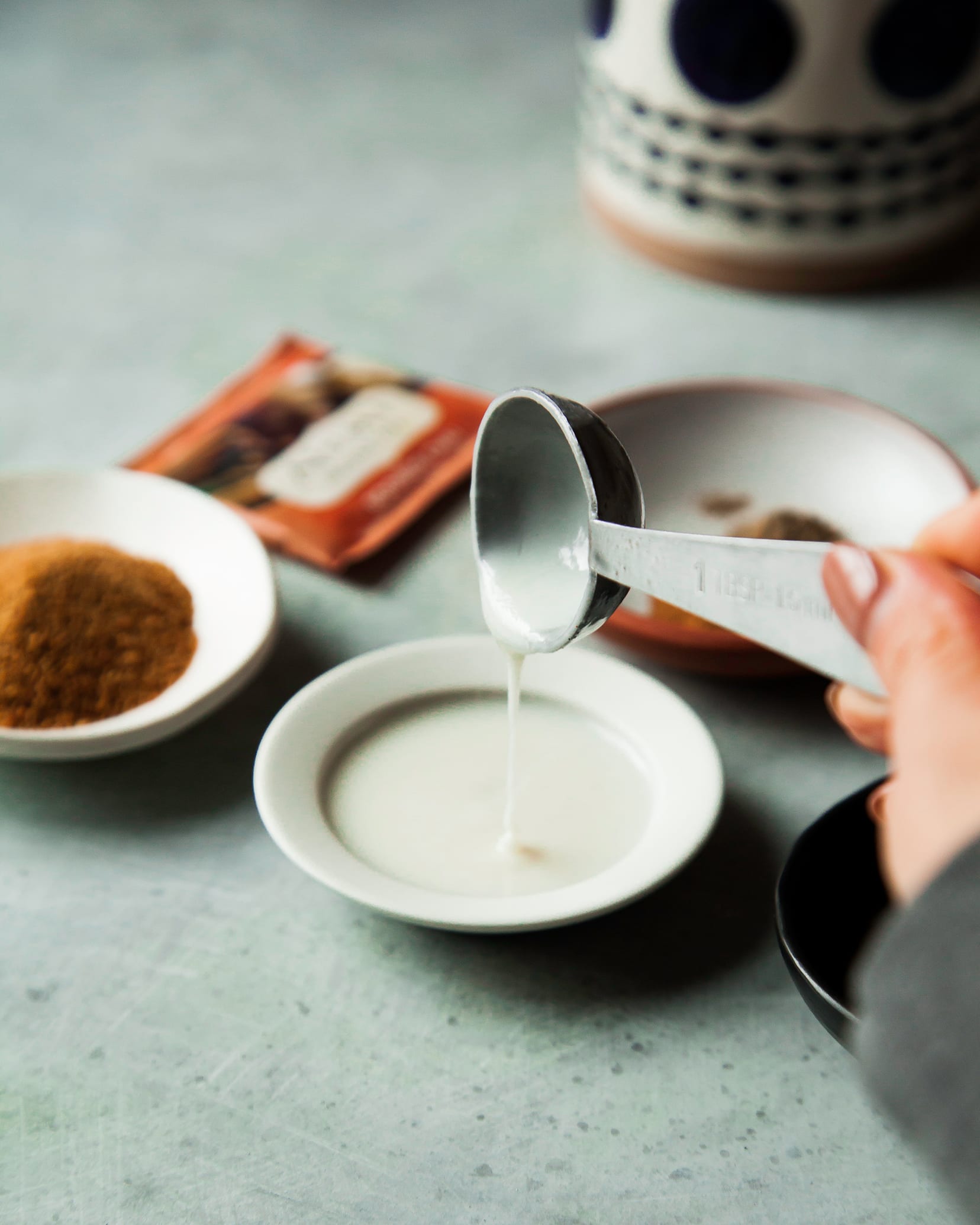 A hand is holding a spoon that is dripping some creamy coconut butter into a dish.