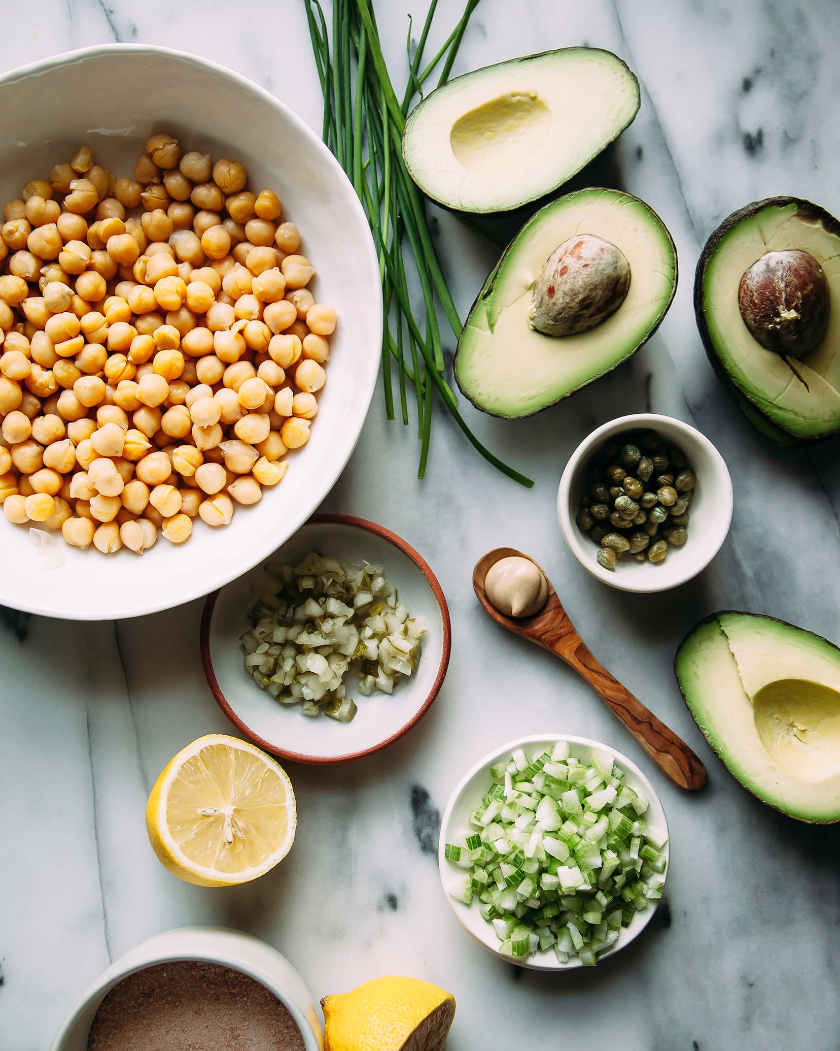 An overhead shot of ingredients for avocado chickpea salad on a grey marble background.