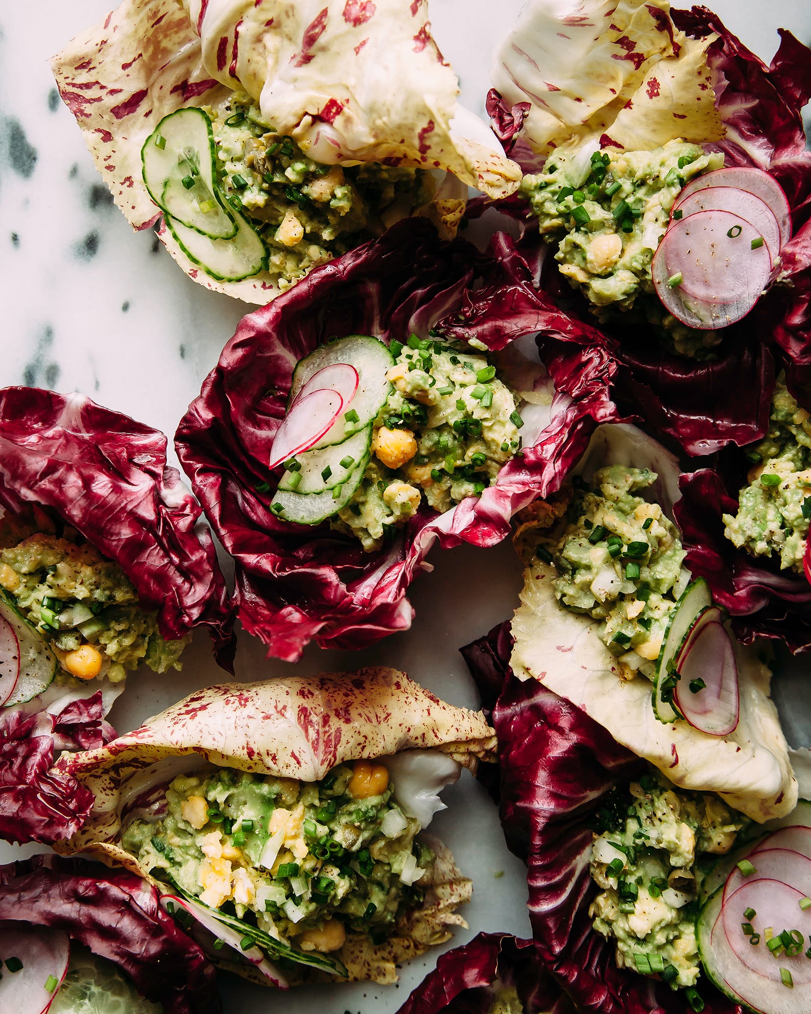 Overhead shot of avocado chickpea salad inside of radicchio lettuce leaves. The salad is light green and sprinkled with chives.