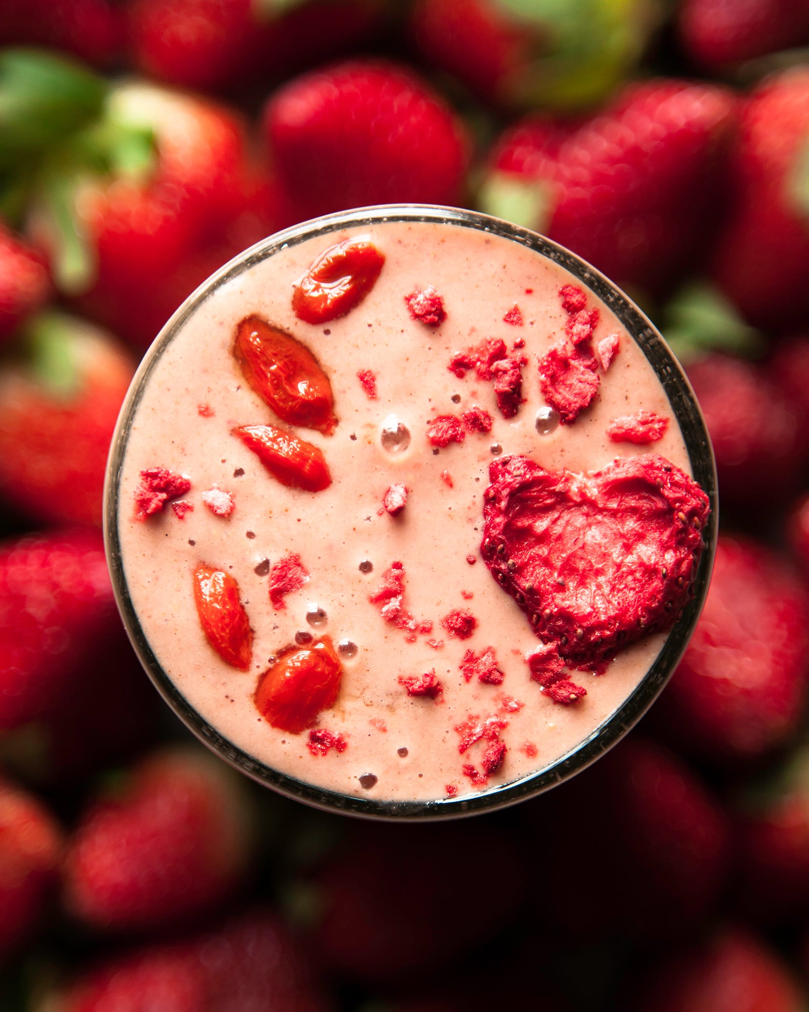 An up close, overhead shot of a light pink strawberry goji smoothie. It is garnished with soaked goji berries and a slice of dehydrated strawberry.