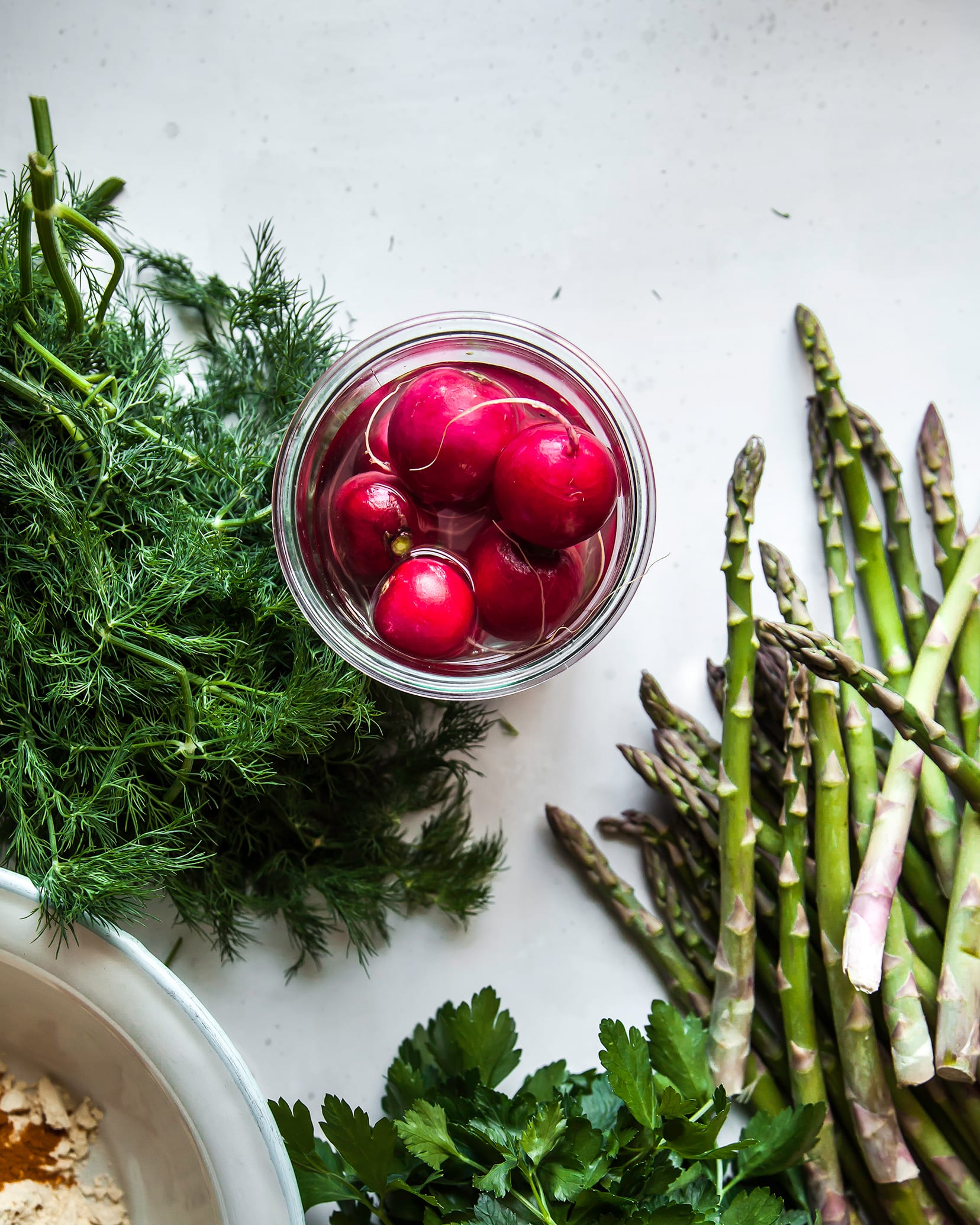 An overhead shot of asparagus, radishes and fresh dill on a white background.