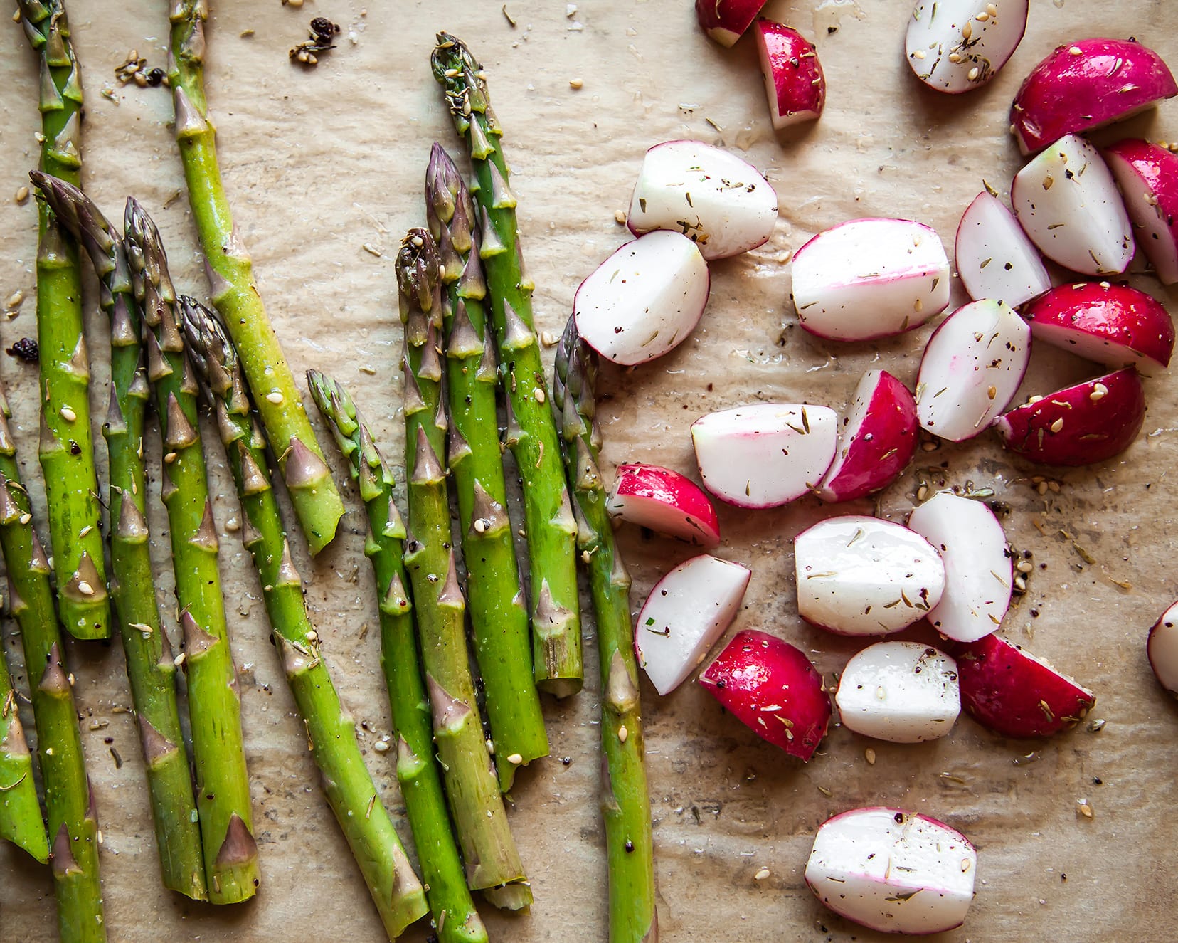 Image shows roasted asparagus and radishes on top of brown parchment paper.