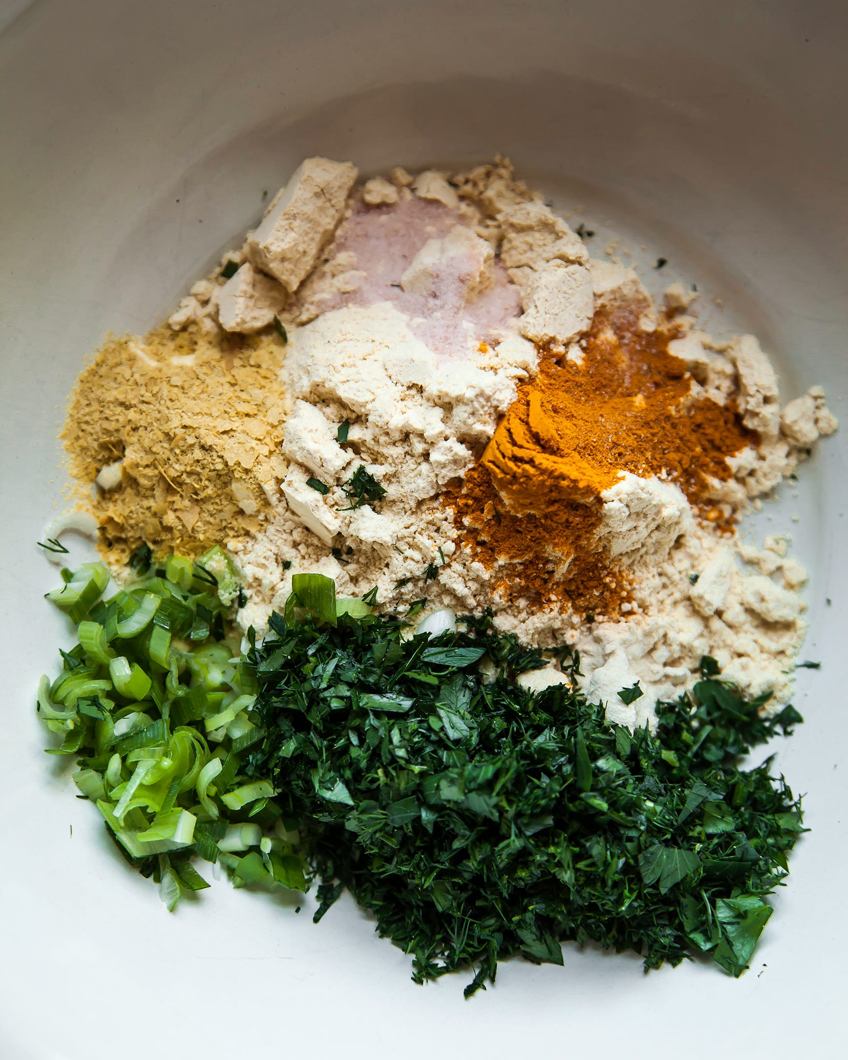 Image is an overhead shot of chickpea flour, herbs, and spices in a bowl.