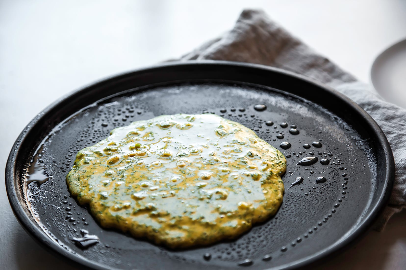 Image shows a yellow and green-flecked pancake being cooked in a greased, shallow skillet.
