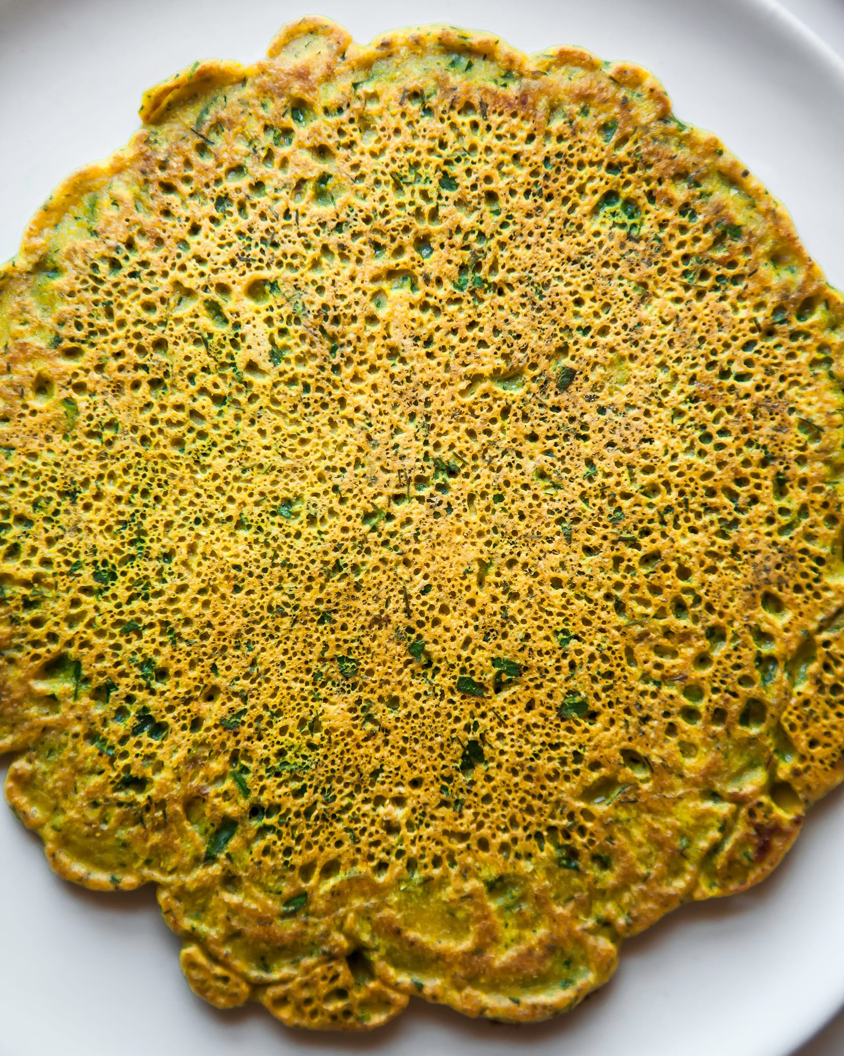 Image is an up close, overhead shot of a yellow and green savoury chickpea flour pancake.