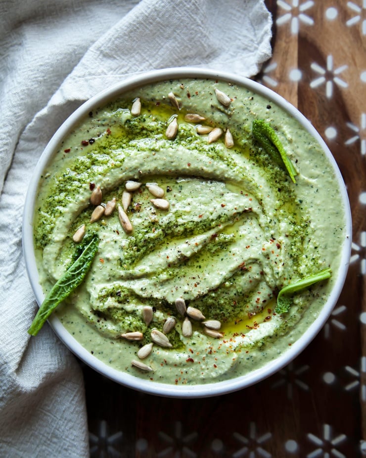 An overhead shot of a creamy, light green kale pesto dip in a bowl.