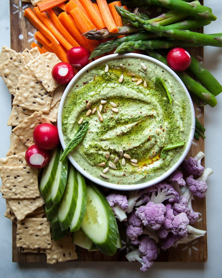 An overhead shot of a creamy light green dip with vegetables served alongside.