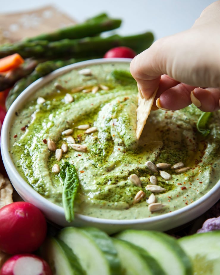 Image shows a hand dipping a cracker into a creamy light green dip.