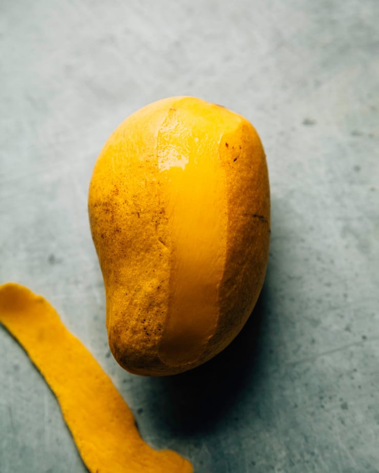 A ripe Ataulfo mango on a pale blue background with a strip of peel removed.