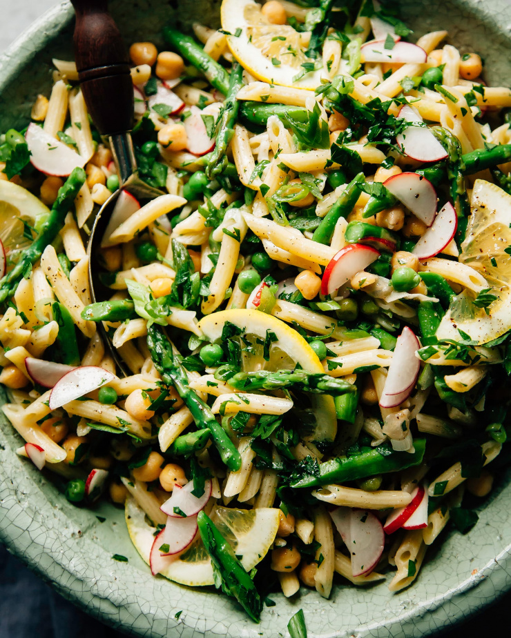 An overhead shot of a pasta salad with lots of green vegetables and herbs in a sage-green ceramic bowl.