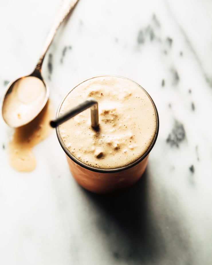 An overhead shot of a very frothy and creamy smoothie inside of a copper tumbler. The tumbler is set on top of a marble background.