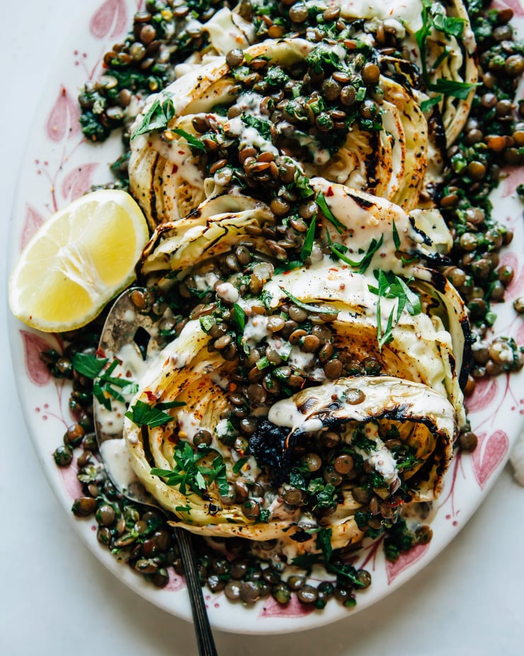 An overhead shot of grilled slices of cabbage with lentils and a creamy sauce on top.