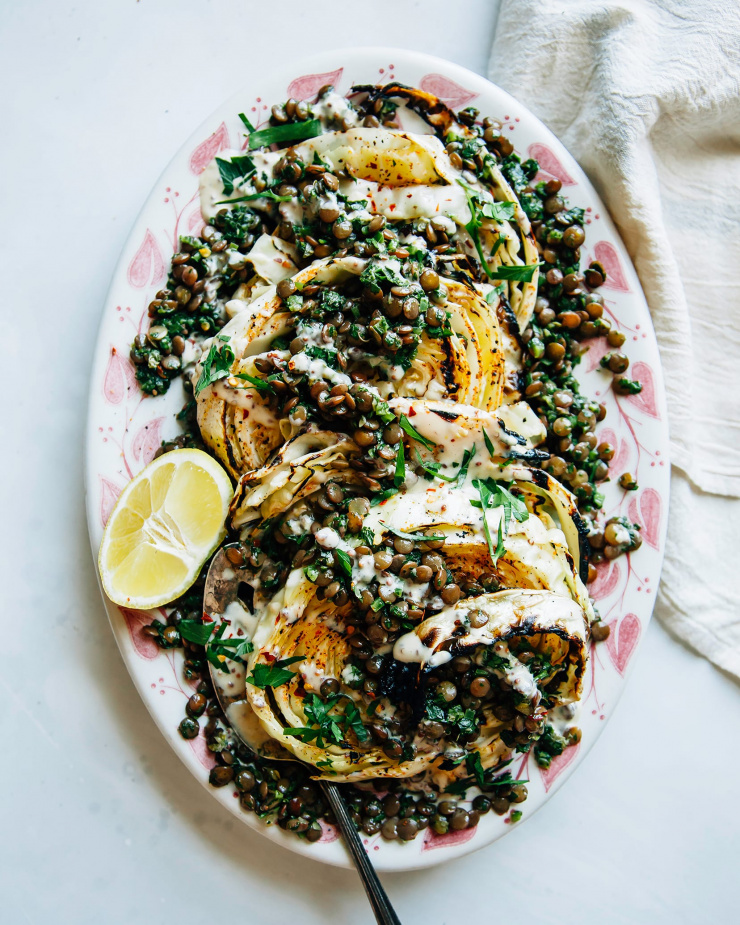 Image shows grilled cabbage steaks topped with lentils, herbs and a creamy sauce.