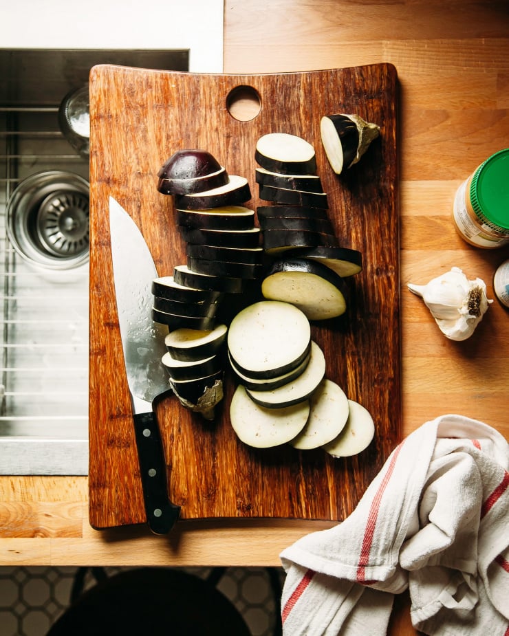 An overhead shot of two sliced eggplants on a wooden cutting board on top of a kitchen counter.