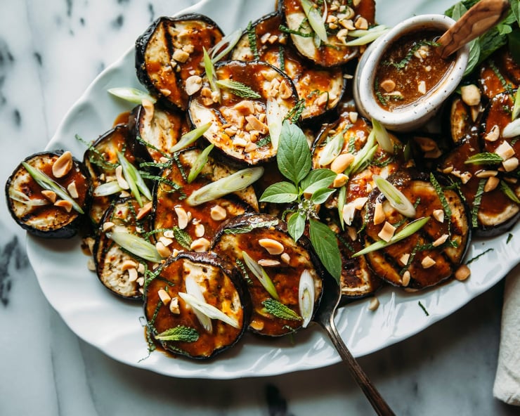 An overhead shot of grilled eggplant slices on a pale blue plate, drizzled with a deep brown sauce and garnished with chopped herbs.