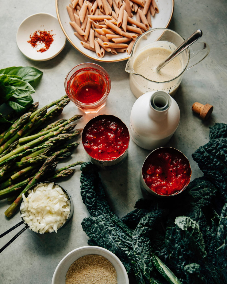 An overhead shot of all ingredients needed for a pasta recipe, all on top of a blue-ish grey background.
