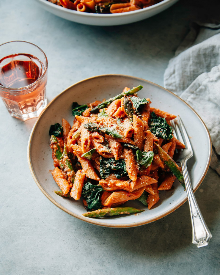 Overhead shot of finished and styled vegan rosé pasta with asparagus and kale. It is in an individual serving bowl with a glass of rosé wine to the side.