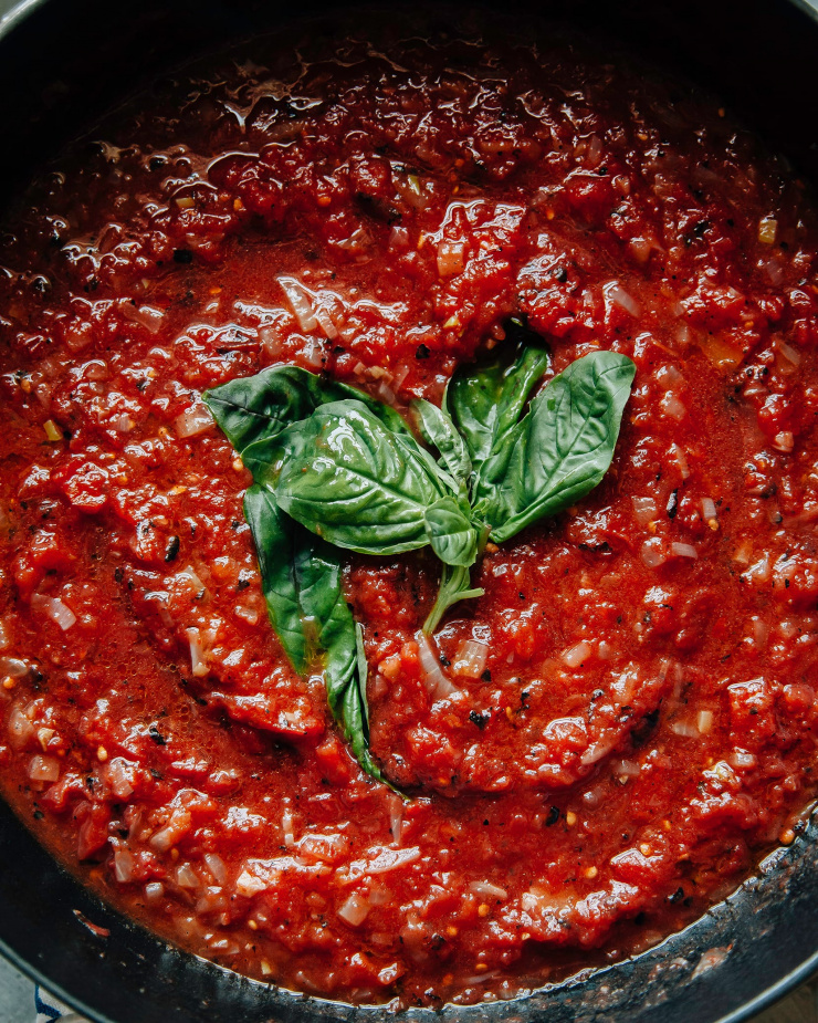 Overhead and up close shot of a basil sprig in the middle of some red sauce.