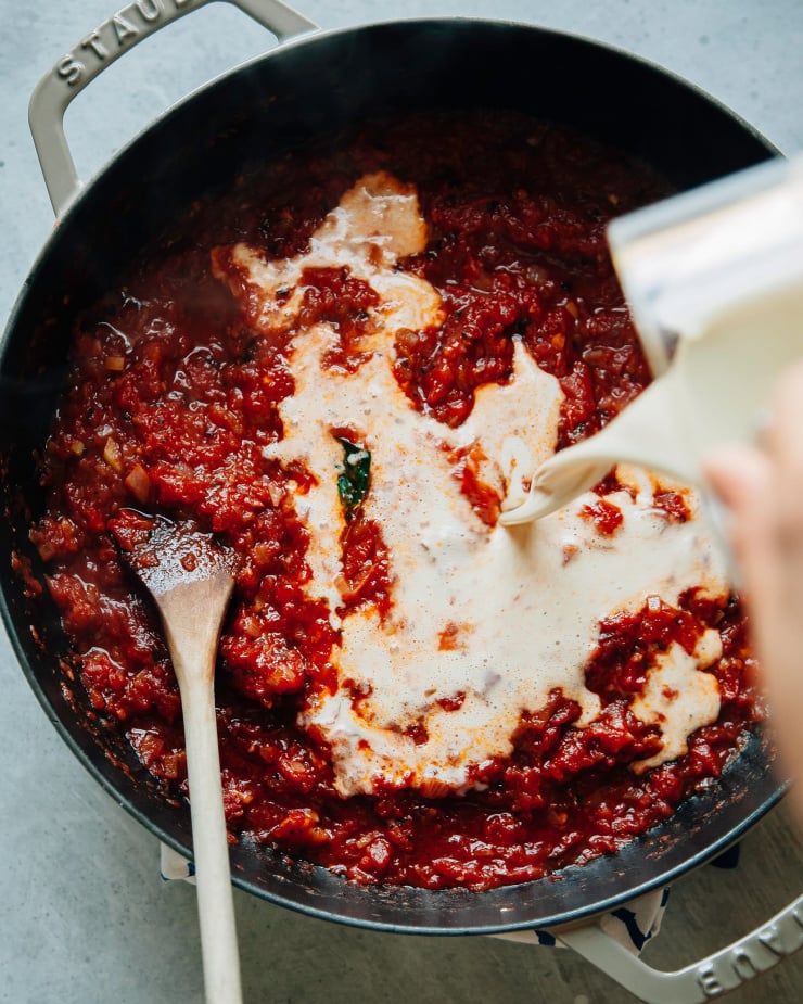Overhead shot of a hand pouring vegan cashew cream into a deep red sauce.