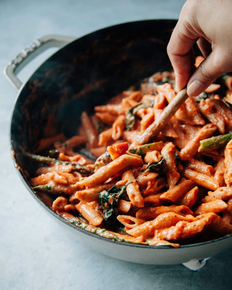 Image shows a creamy pasta being stirred and combined in a pot.