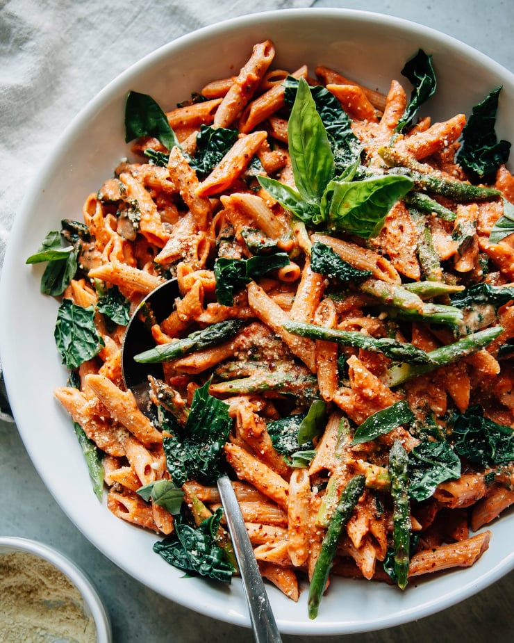 Overhead shot of finished and styled rosé pasta with asparagus and kale. It is served in a large white bowl.
