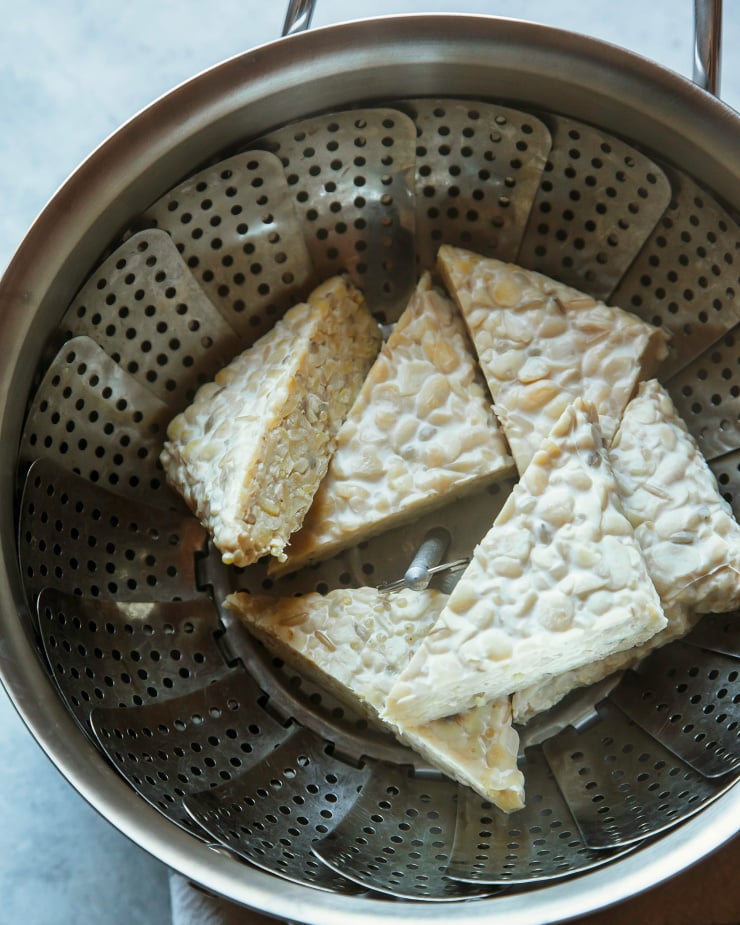 Image shows triangular pieces of tempeh in a steamer basket.
