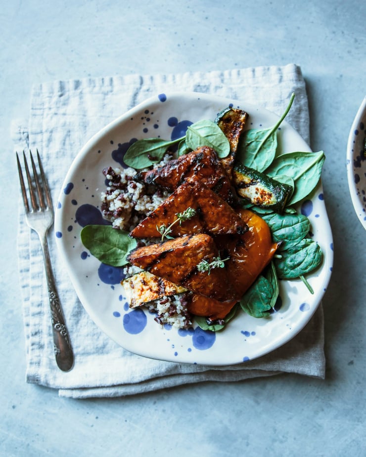 An overhead shot showing marinated and grilled tempeh pieces on a bed of cooked grains and greens.