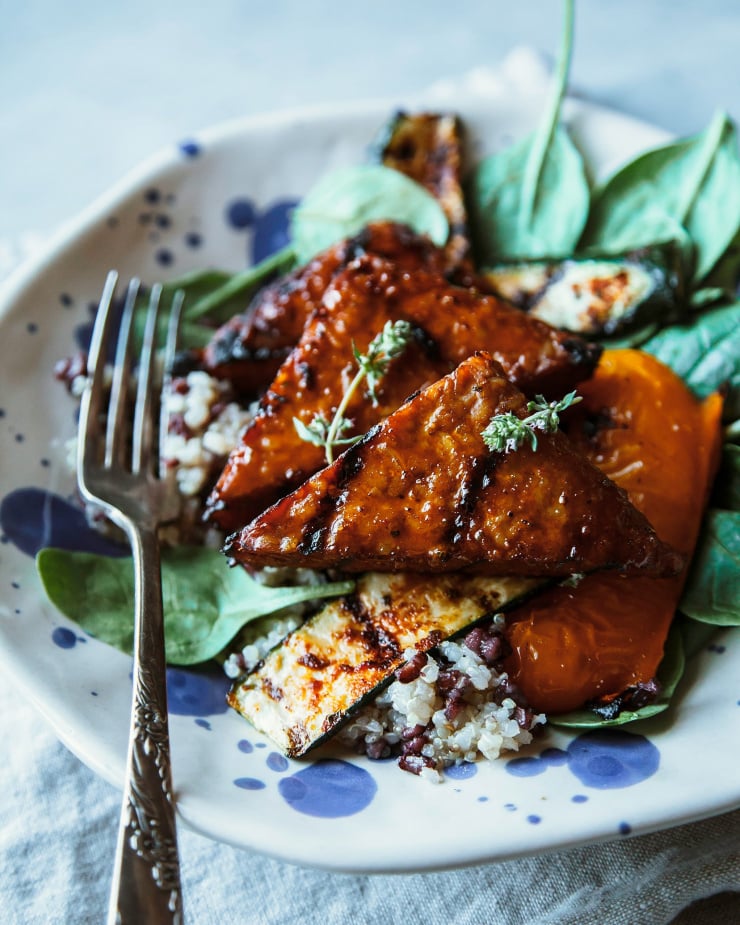A 3/4 angle shot showing marinated and grilled tempeh pieces on a bed of cooked grains and greens.