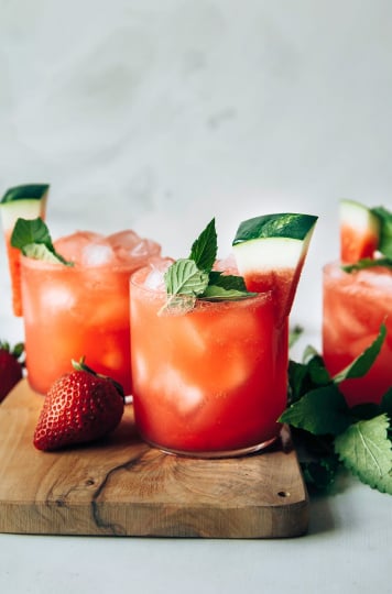 Photo displays finished glasses of sparkling strawberry watermelon limeade, garnished with wedges of watermelon and mint.