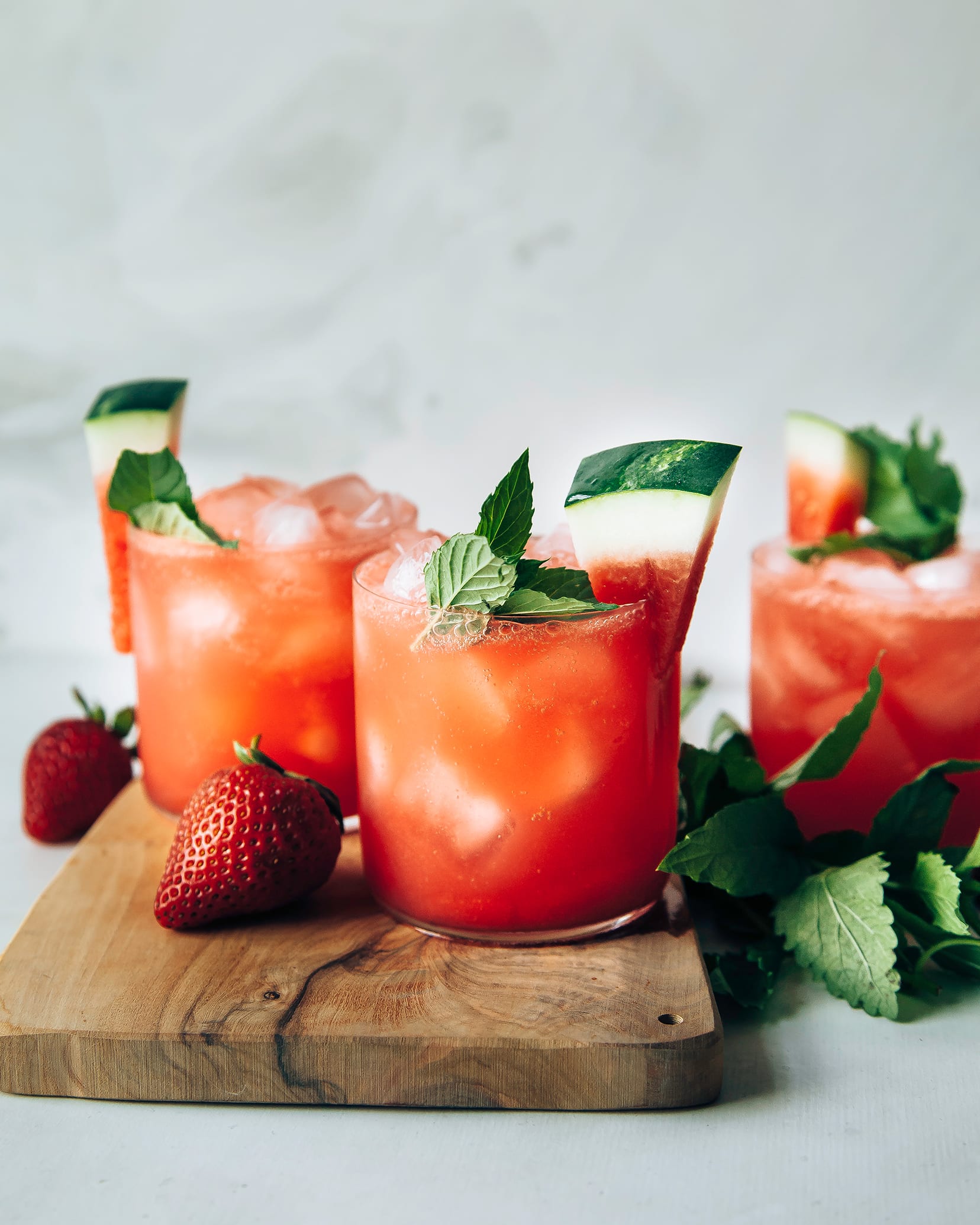 Photo displays finished glasses of sparkling strawberry watermelon limeade, garnished with wedges of watermelon and mint.