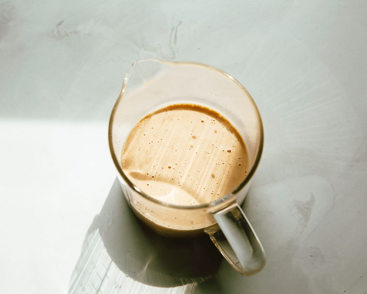 A creamy peanut butter lime dressing photographed in a glass measuring cup in harsh, natural light.