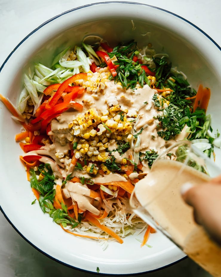 An overhead shot of charred corn slaw with peanut butter lime dressing being poured over top, pre-mixing.