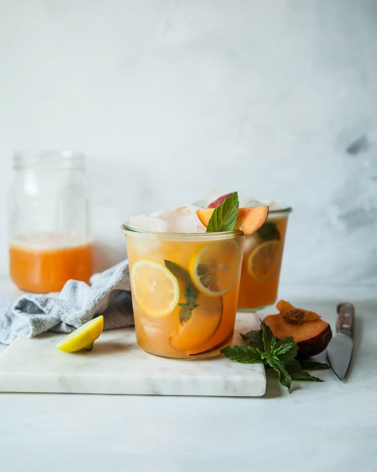 A head on shot of iced peach green tea in clear glass wide mouth jars against a marble backdrop.