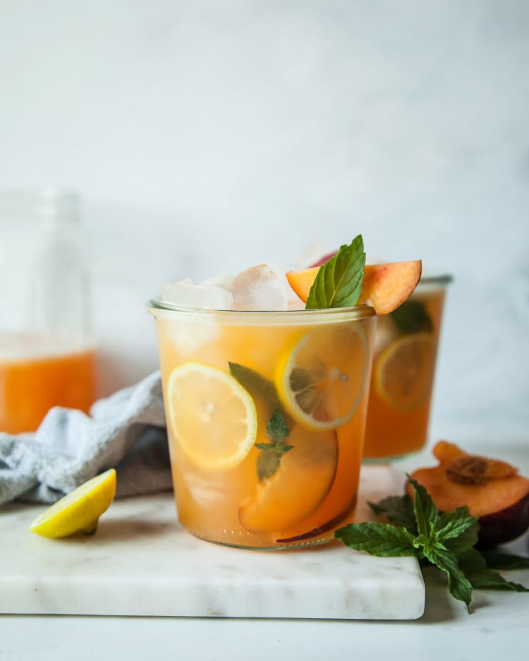 A head on shot of iced peach green tea in clear glass wide mouth jars against a marble backdrop.