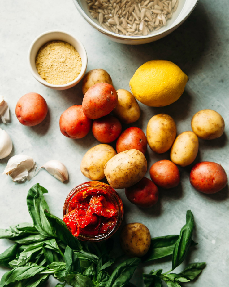 An overhead shot of ingredients for smashed potatoes with sunflower seed-based Caesar drizzle. All ingredients are on a light blue-grey background.