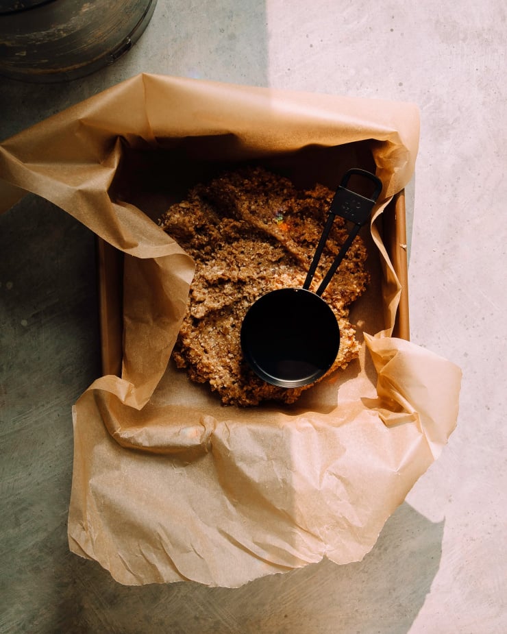 A paper lined baking pan has lemon bar crust inside of it, before being pressed in evenly. The photo is taken in direct sunlight.