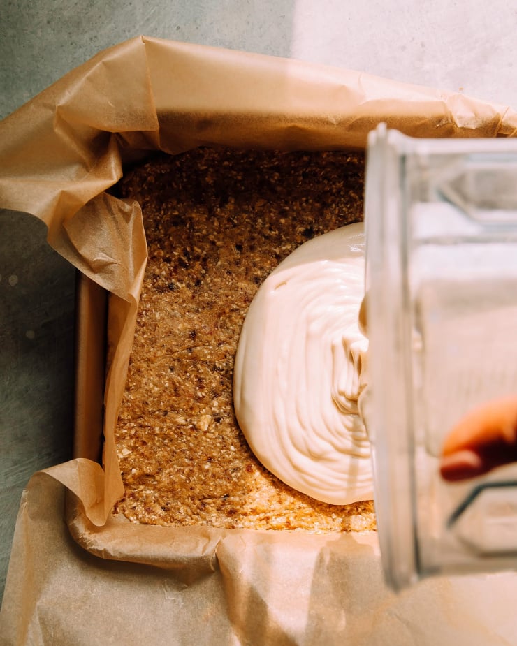 Lemon filling being poured from a blender pitcher on top of a crust in a square baking pan.