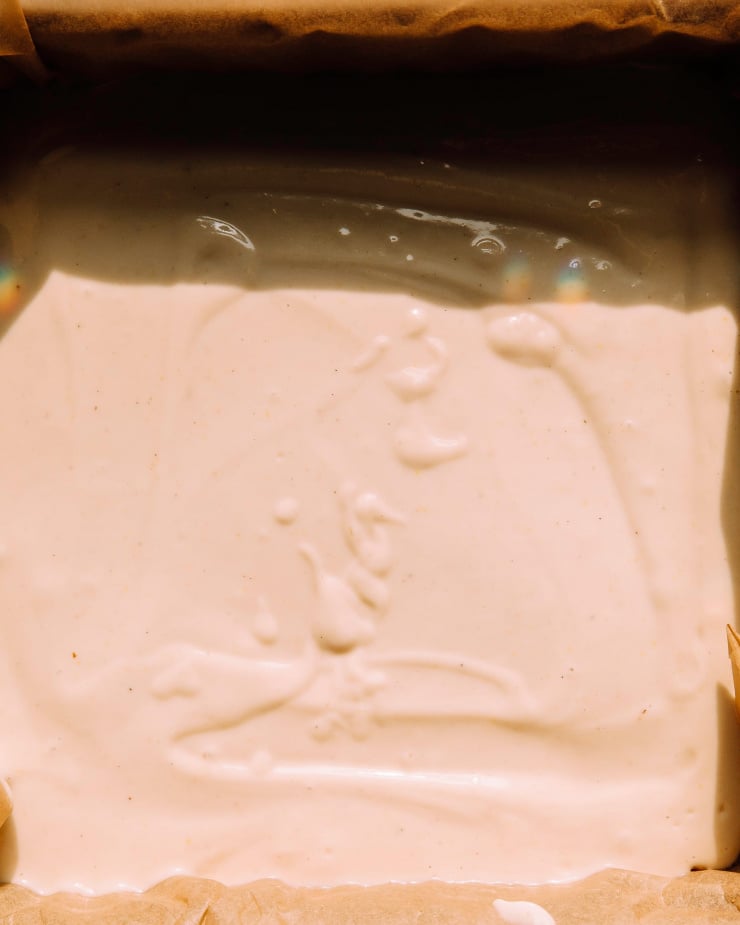 AN up close, overhead shot of lemon filling poured into a prepared pan in direct sunlight with stark contrast.