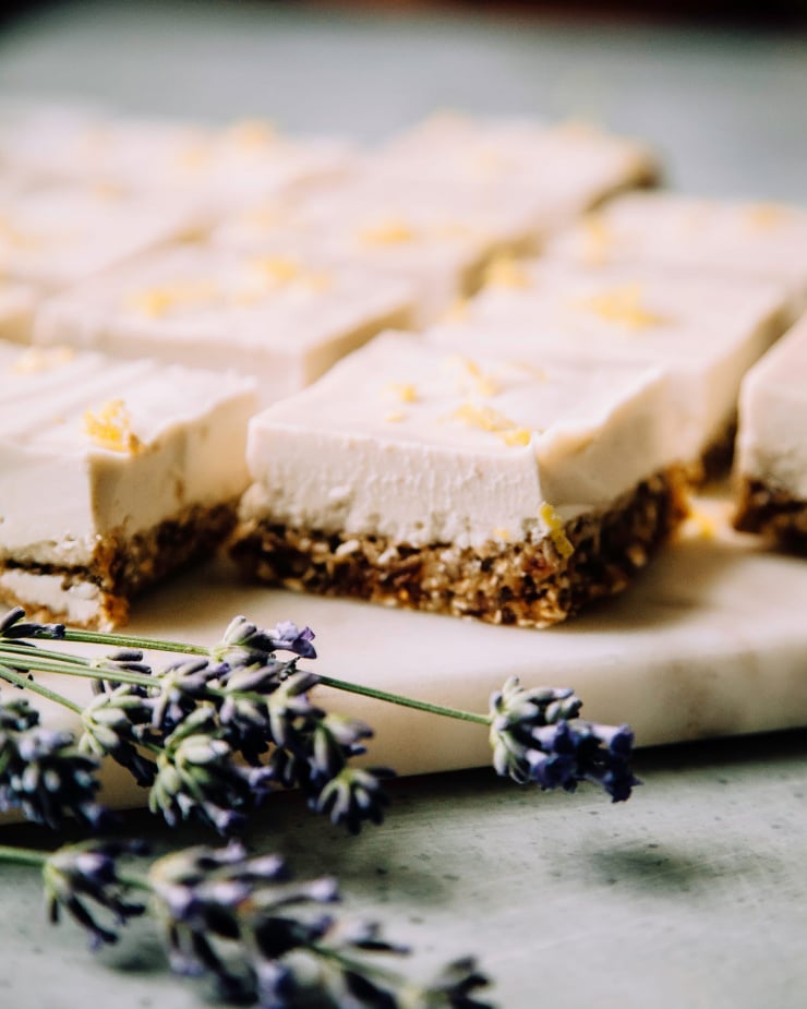 A side angle shot of creamy vegan lemon bars on a marble board with a few sprigs of lavender nearby.