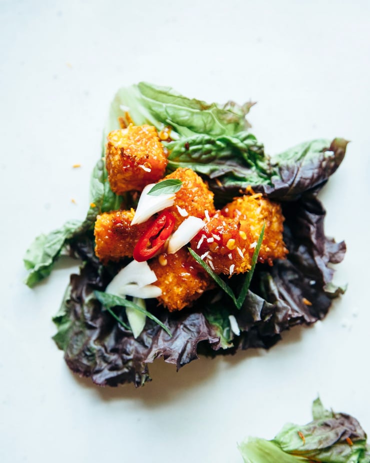 An overhead shot of a singular crispy coconut tofu lettuce wrap. The tofu is wrapped in red leaf lettuce and the cubes of tofu are deep golden brown.