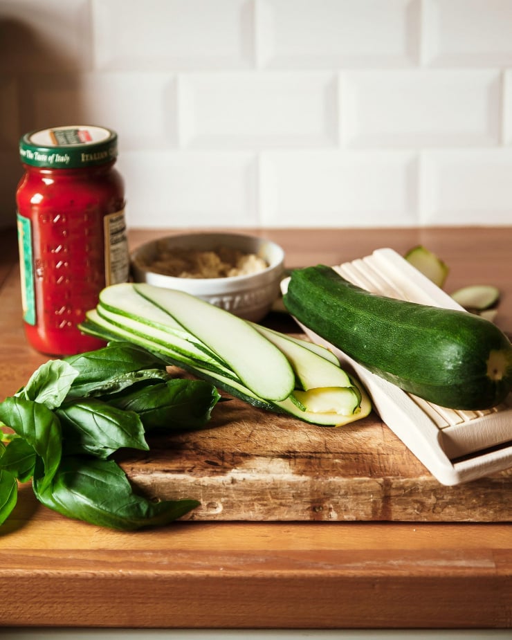 A side angle shot of ingredients for zucchini Involtini on top of a butcher block kitchen counter with white tile in the background.