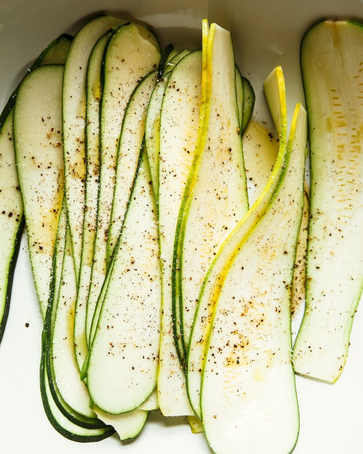 An overhead shot of very thin zucchini slices, seasoned with salt and pepper.