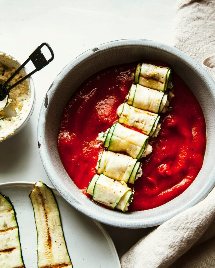 An overhead shot of zucchini Involtini being rolled up, assembled and placed in a baking dish with marinara.
