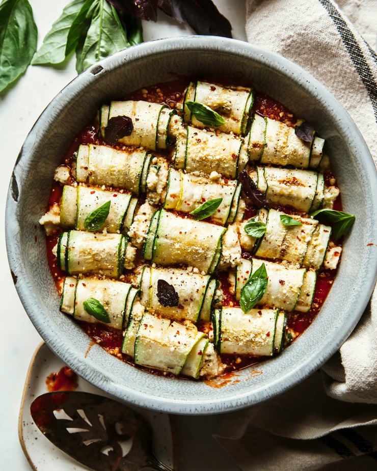 An overhead shot of zucchini Involtini with almond ricotta in a grey enamelware baking dish on top of a white background.
