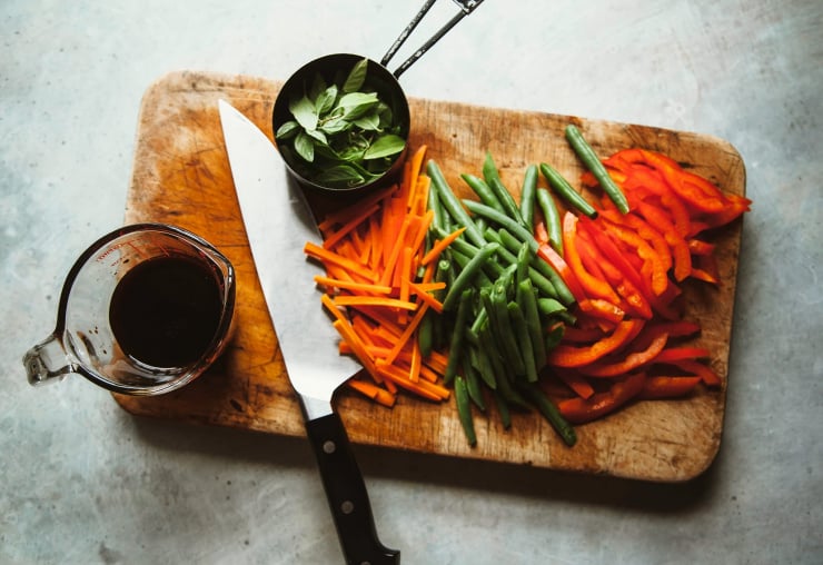 Image shows sliced vegetables on a cutting board along with a cup of Thai basil leaves.