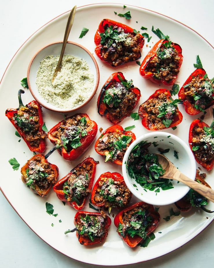 An overhead shot of a platter of mini red peppers cut in half and stuffed with a meaty, plant-based mixture and topped with chopped herbs. Part of a roundup of vegan appetizer recipes.