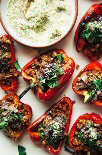 HAlves of red bell pepper are facing up on a platter and are stuffed with a lentil and walnut mixture and topped with chopped parsley and finely ground hemp seed mixture.