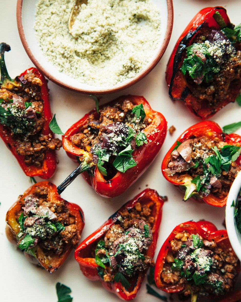 HAlves of red bell pepper are facing up on a platter and are stuffed with a lentil and walnut mixture and topped with chopped parsley and finely ground hemp seed mixture.