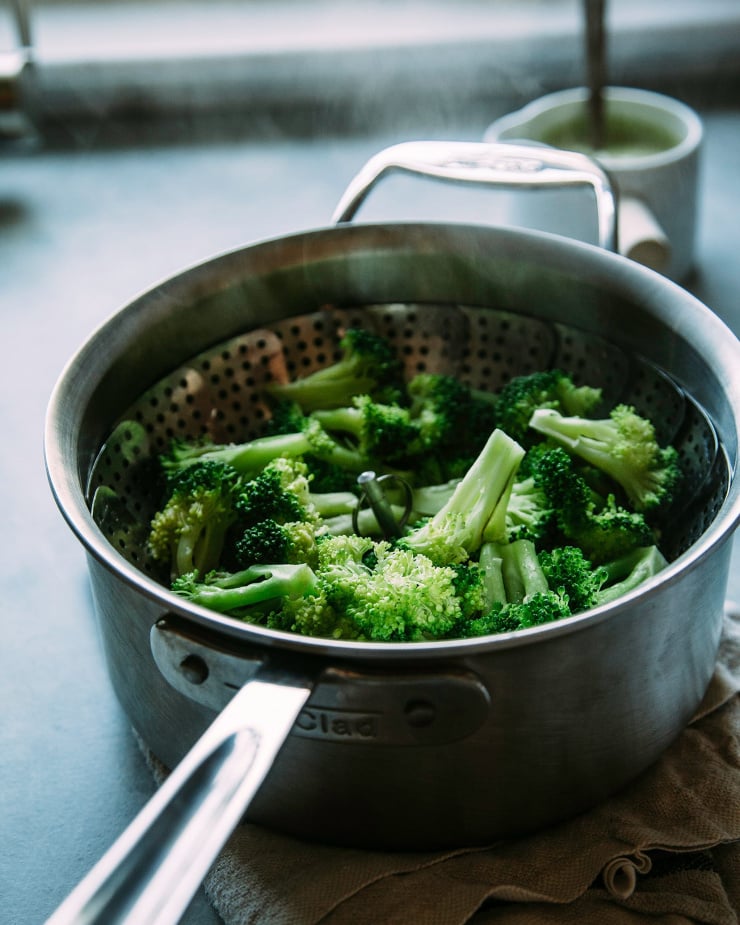 A 3/4 angle shot of some broccoli steaming in a stainless steel saucepan.