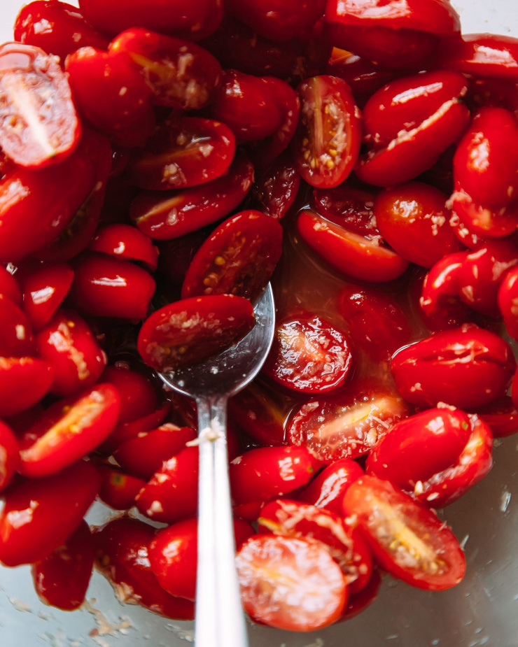 An up close, overhead shot of halved grape tomatoes marinating in seasoning and olive oil.